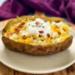 smoked baked potatoes on a plate loaded with sour cream, cheese, and bacon