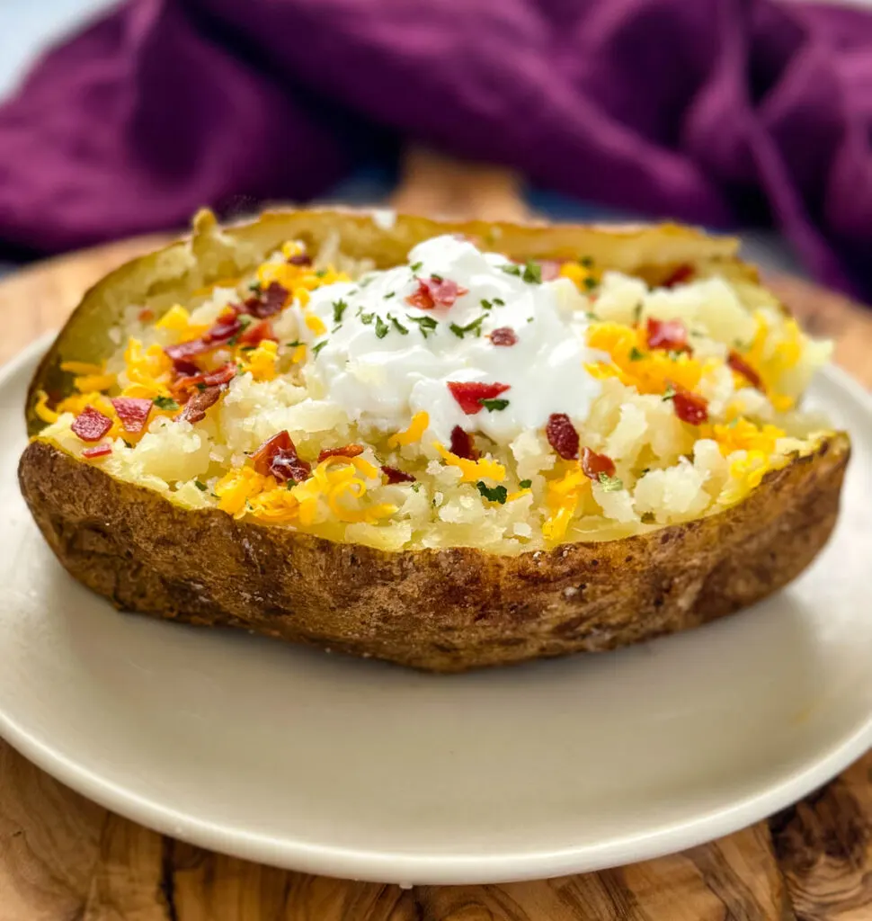 smoked baked potatoes on a plate loaded with sour cream, cheese, and bacon