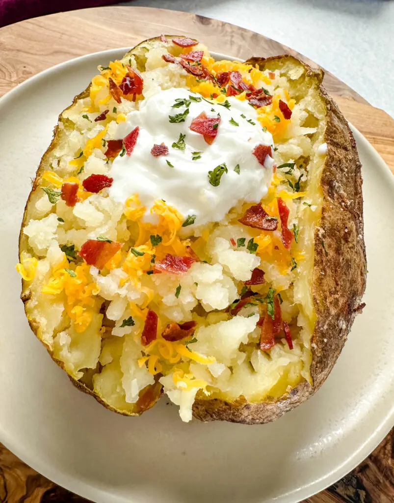 smoked baked potatoes on a plate loaded with sour cream, cheese, and bacon