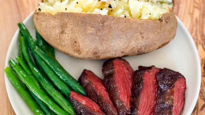 smoked filet mignon on a plate with green beans and a baked potato