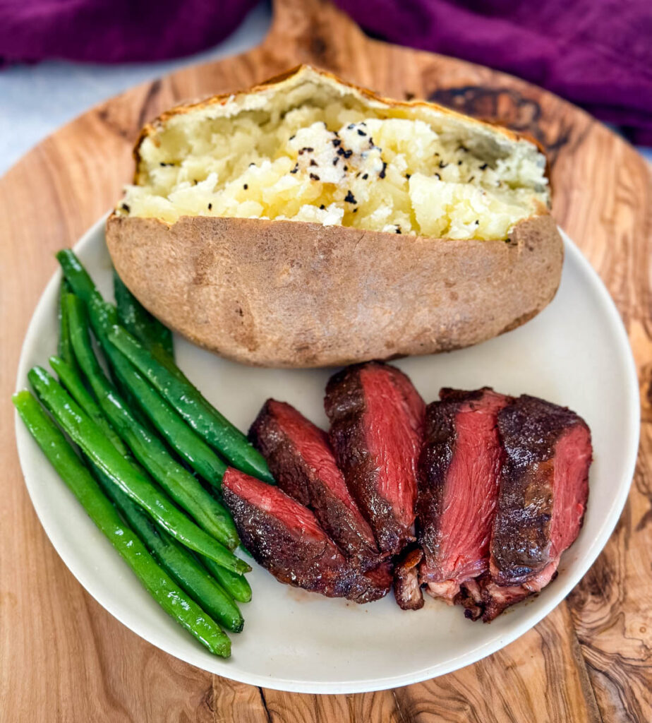 smoked filet mignon on a plate with green beans and a baked potato