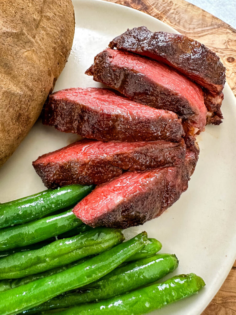 smoked filet mignon on a plate with green beans and a baked potato