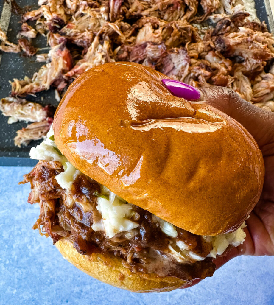 person holding smoked pulled pork sandwich