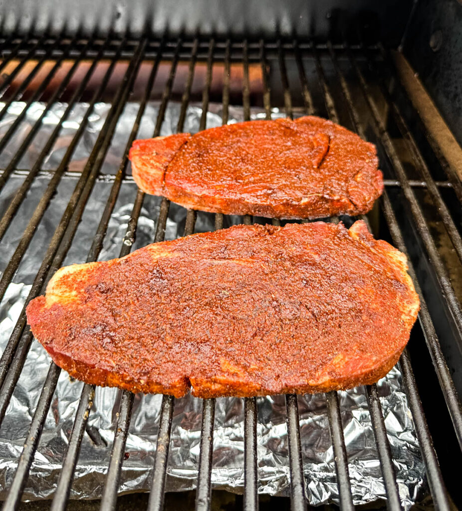 raw seasoned ribeye steak on a Traeger smoker grill