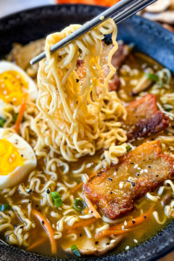 person holding chop sticks with pork belly ramen in a bowl