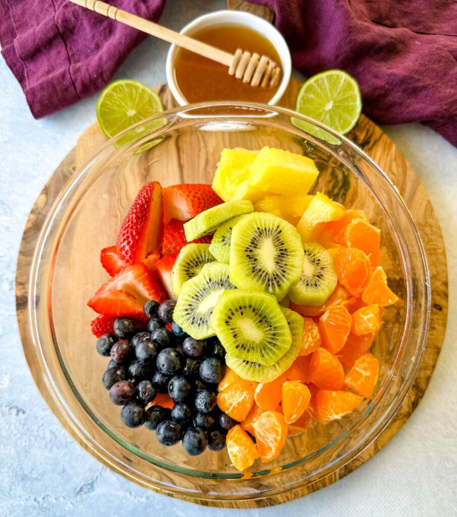 fresh strawberries, mandarin oranges, kiwi, blueberries, and pineapple in a glass bowl