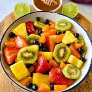 fresh strawberries, mandarin oranges, kiwi, blueberries, and pineapple fruit salad in a white bowl with honey lime dressing