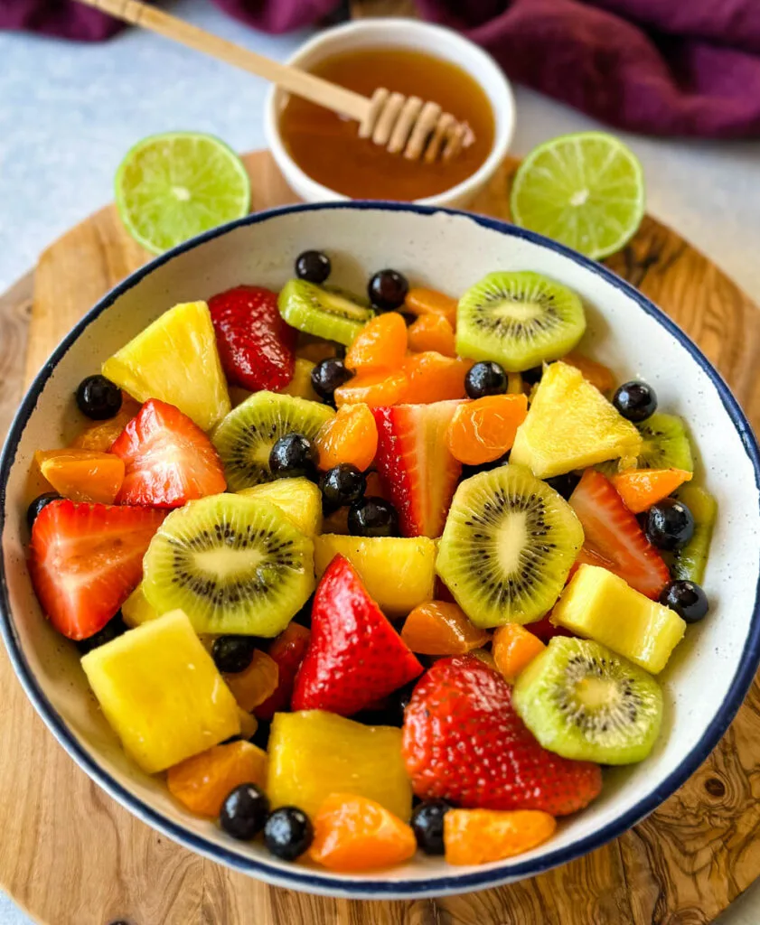 fresh strawberries, mandarin oranges, kiwi, blueberries, and pineapple fruit salad in a white bowl with honey lime dressing