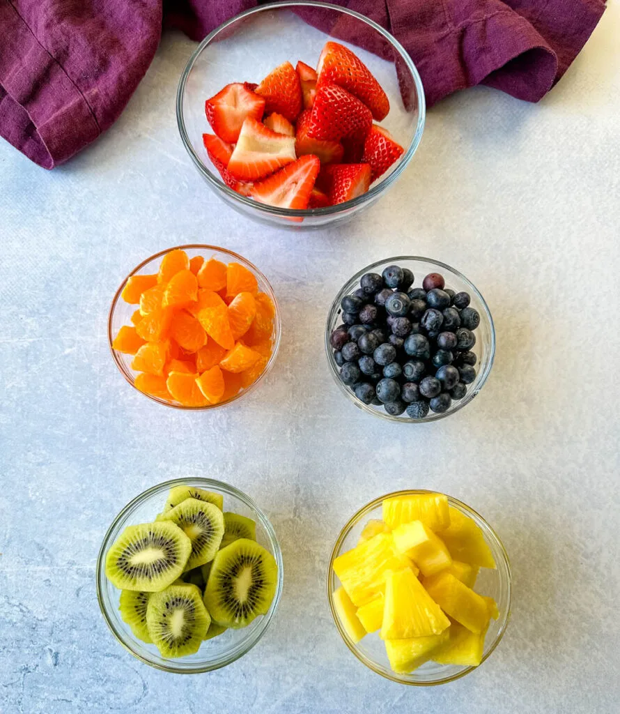 fresh strawberries, mandarin oranges, kiwi, blueberries, and pineapple sliced and in separate glass bowls