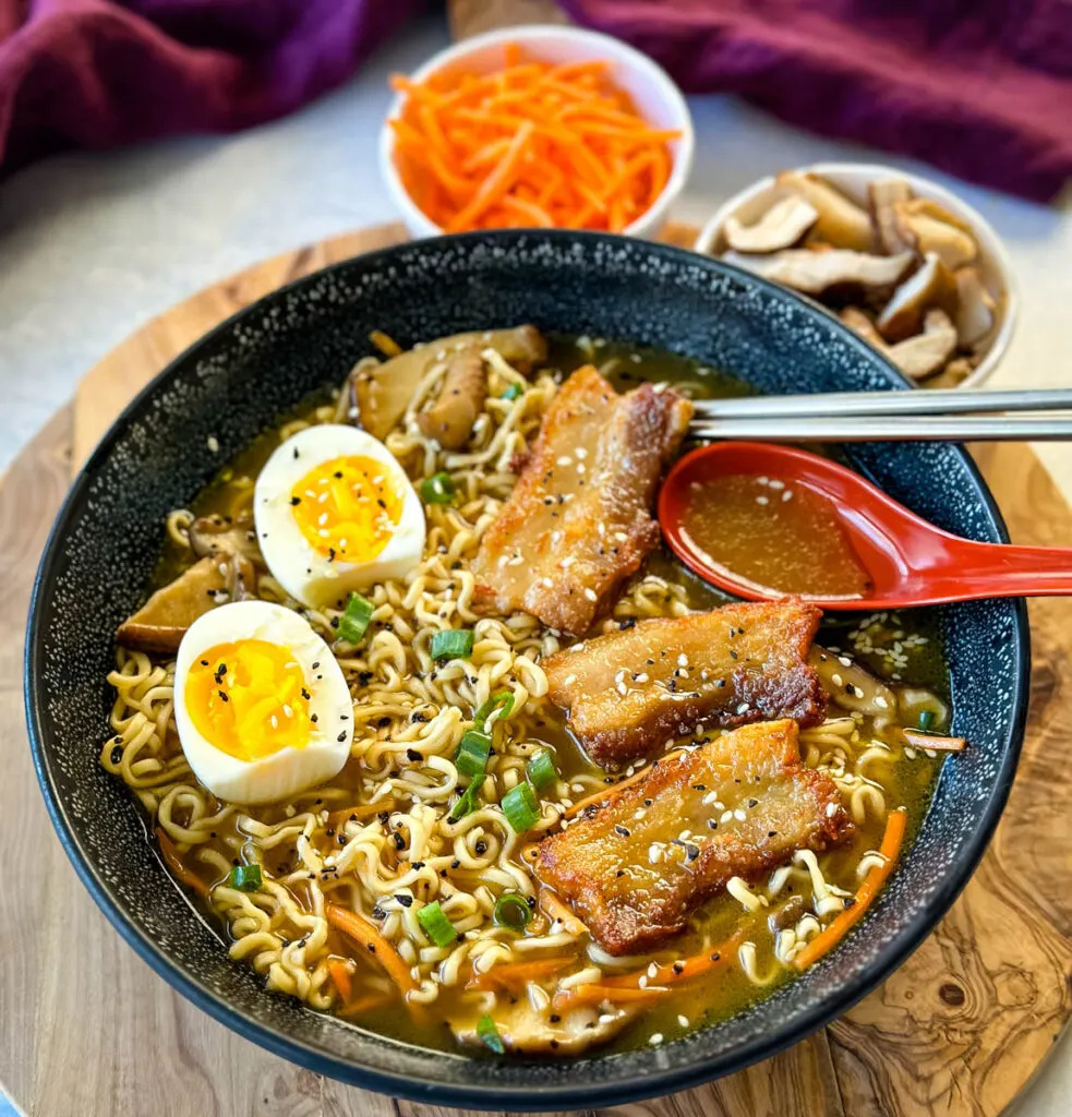 pork belly ramen with soft boiled eggs, green onions, and sesame seeds in a bowl