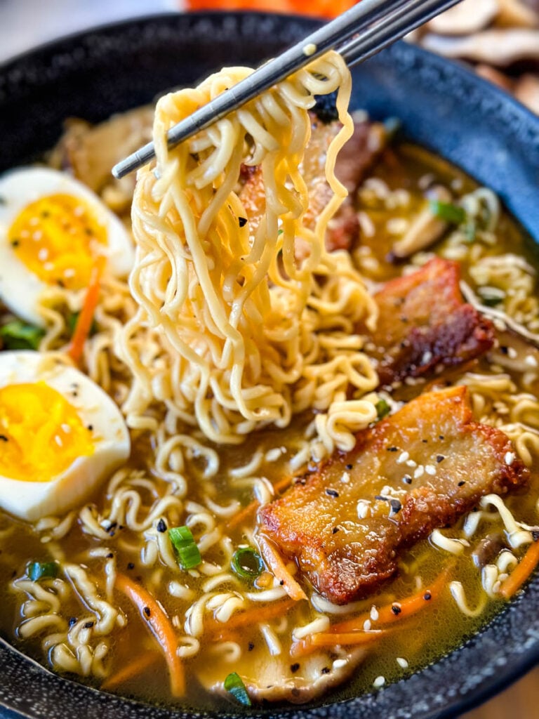 person holding chop sticks with pork belly ramen in a bowl