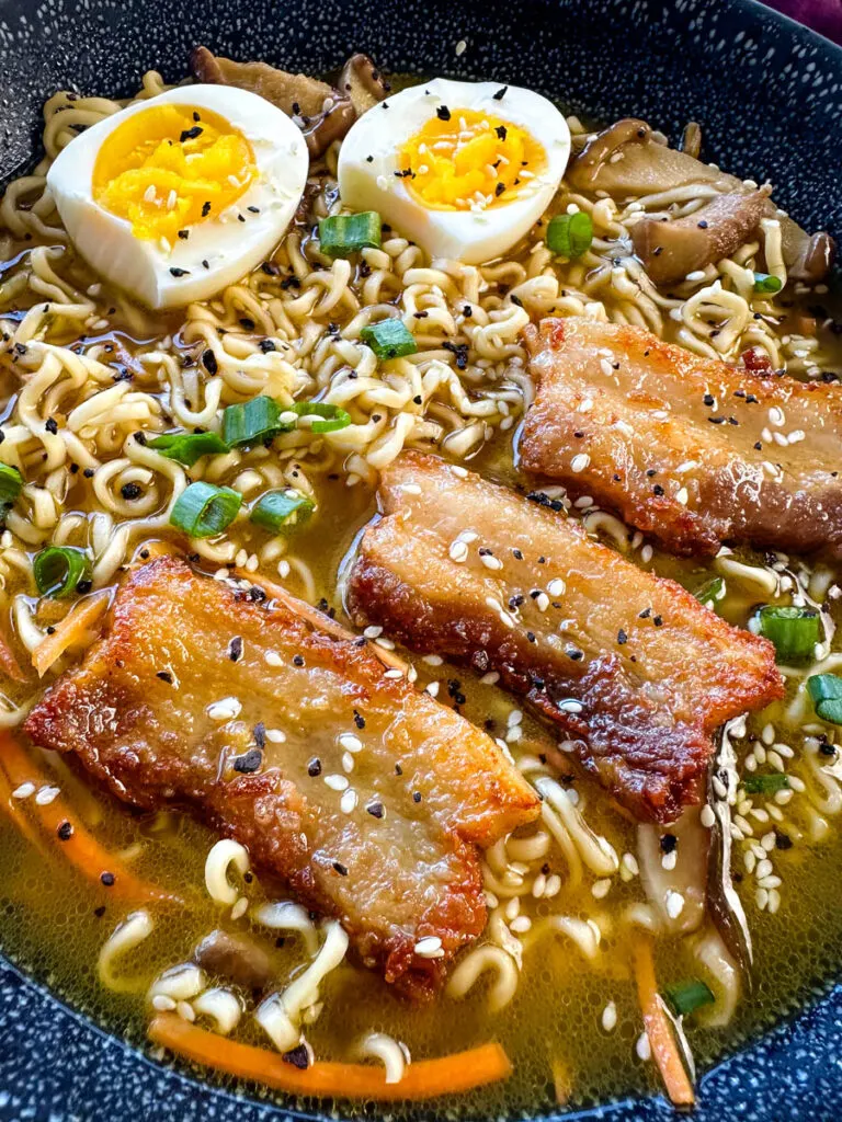 pork belly ramen with soft boiled eggs, green onions, and sesame seeds in a bowl