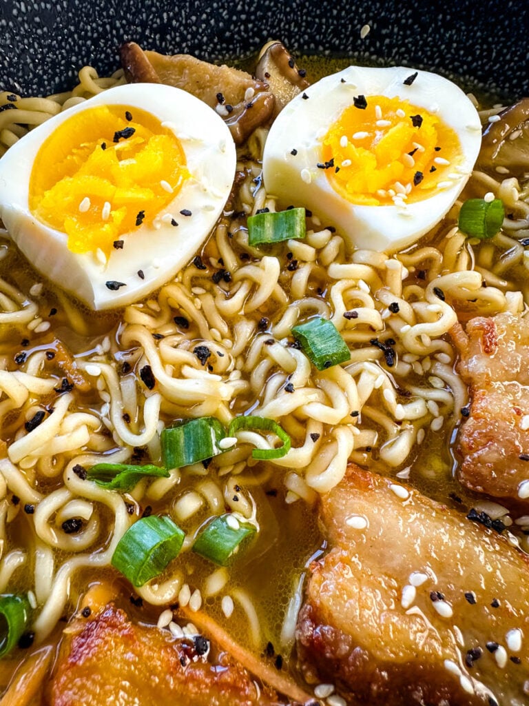 pork belly ramen with soft boiled eggs, green onions, and sesame seeds in a bowl