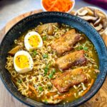 pork belly ramen with soft boiled eggs, green onions, and sesame seeds in a bowl