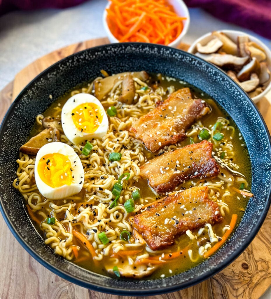 pork belly ramen with soft boiled eggs, green onions, and sesame seeds in a bowl