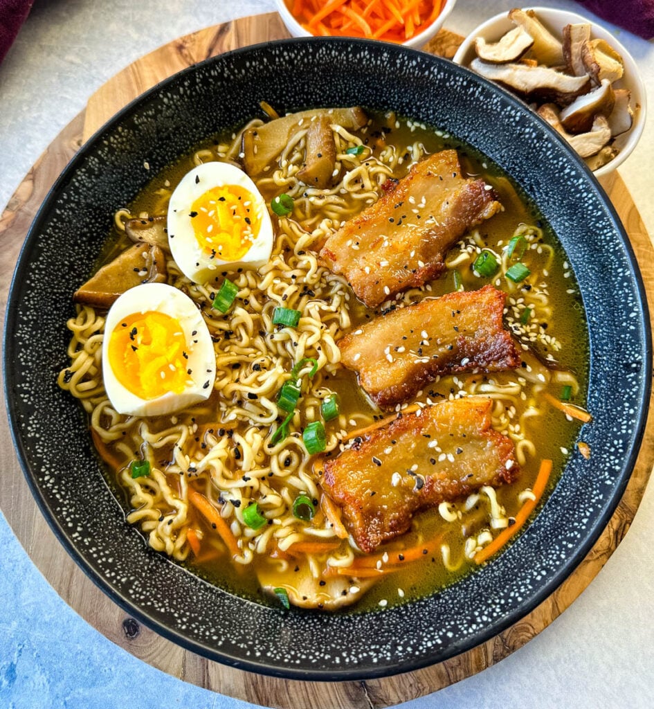 pork belly ramen with soft boiled eggs, green onions, and sesame seeds in a bowl
