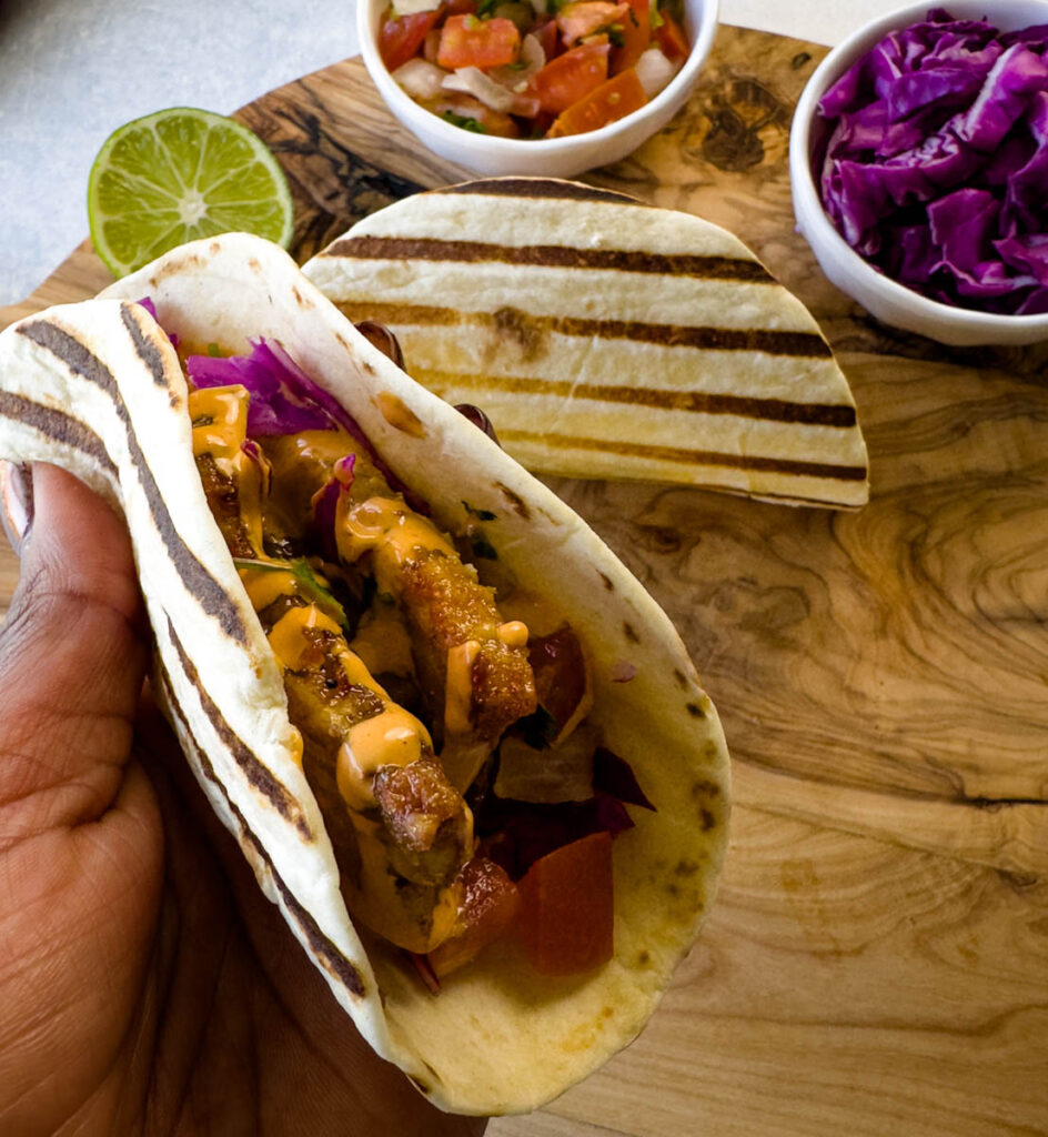 person holding pork belly taco with seared flour tortilla