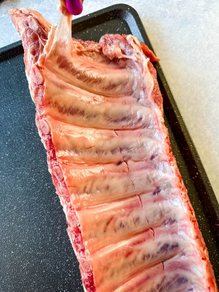 person removing membrane from the back of raw pork ribs on a flat surface