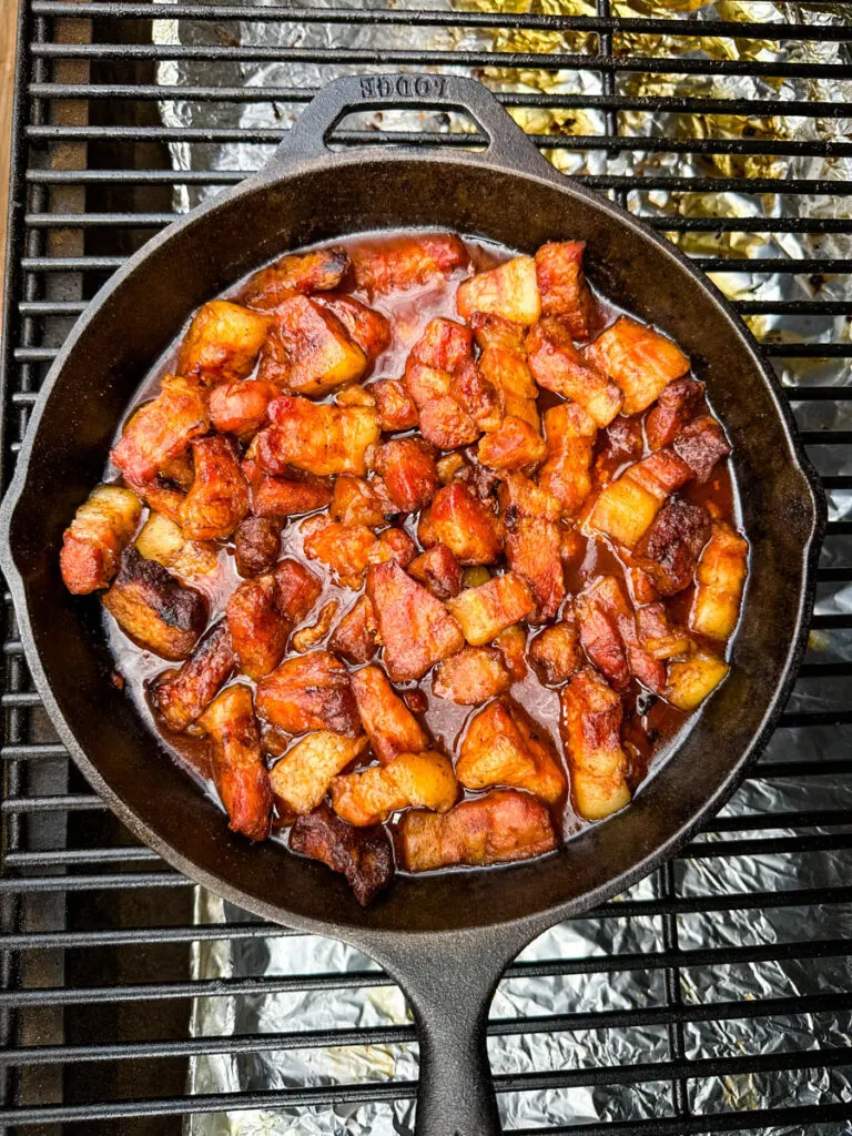pork belly burnt ends and BBQ sauce in a cast iron skillet on a Traeger smoker grill