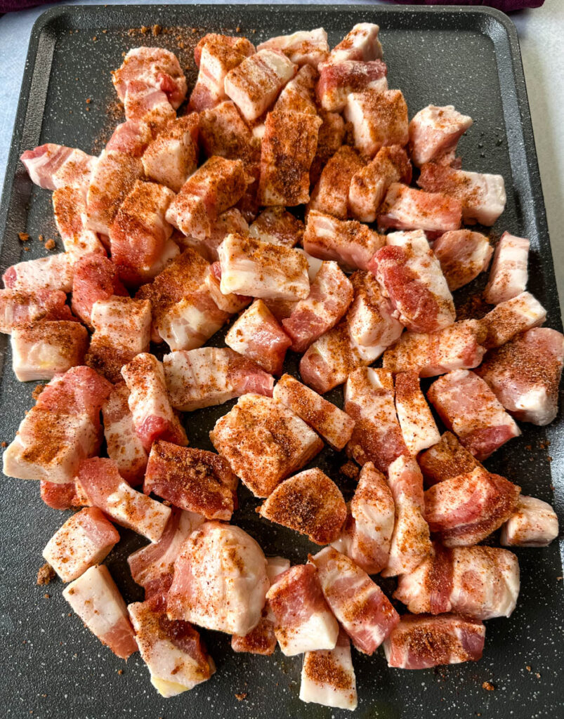 raw seasoned pork belly cut into chunks on a sheet pan