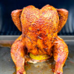 cooked, smoked seasoned whole chicken on a beer can in a Traeger smoker pellet grill