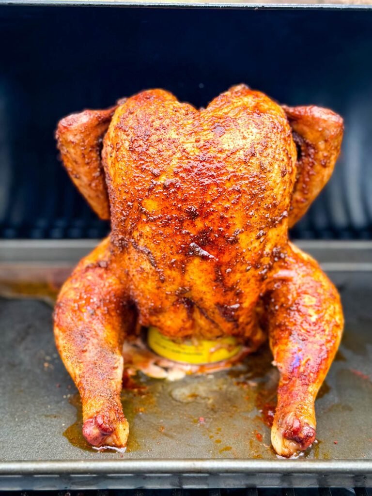 cooked, smoked seasoned whole chicken on a beer can in a Traeger smoker pellet grill