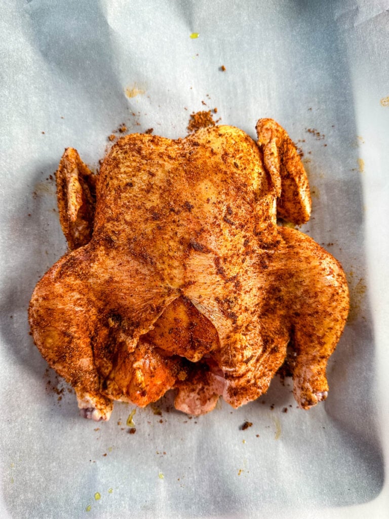 raw seasoned whole chicken on parchment paper