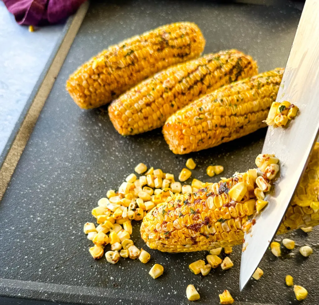 knife cutting Traeger smoked corn on the cob with garlic butter on a sheet pan