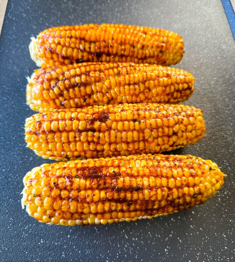 fresh corn on the cob ears on a sheet pan with smoked garlic butter and spices