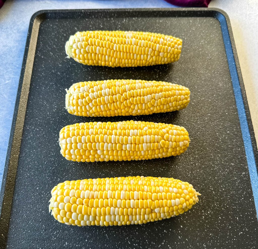 fresh corn on the cob ears on a sheet pan