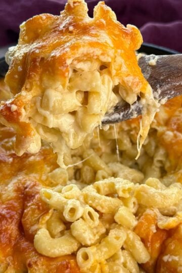 Close-up of a cast iron skillet filled with Southern baked mac and cheese, with a wooden spoon lifting a gooey serving showing melted cheddar cheese stretching.