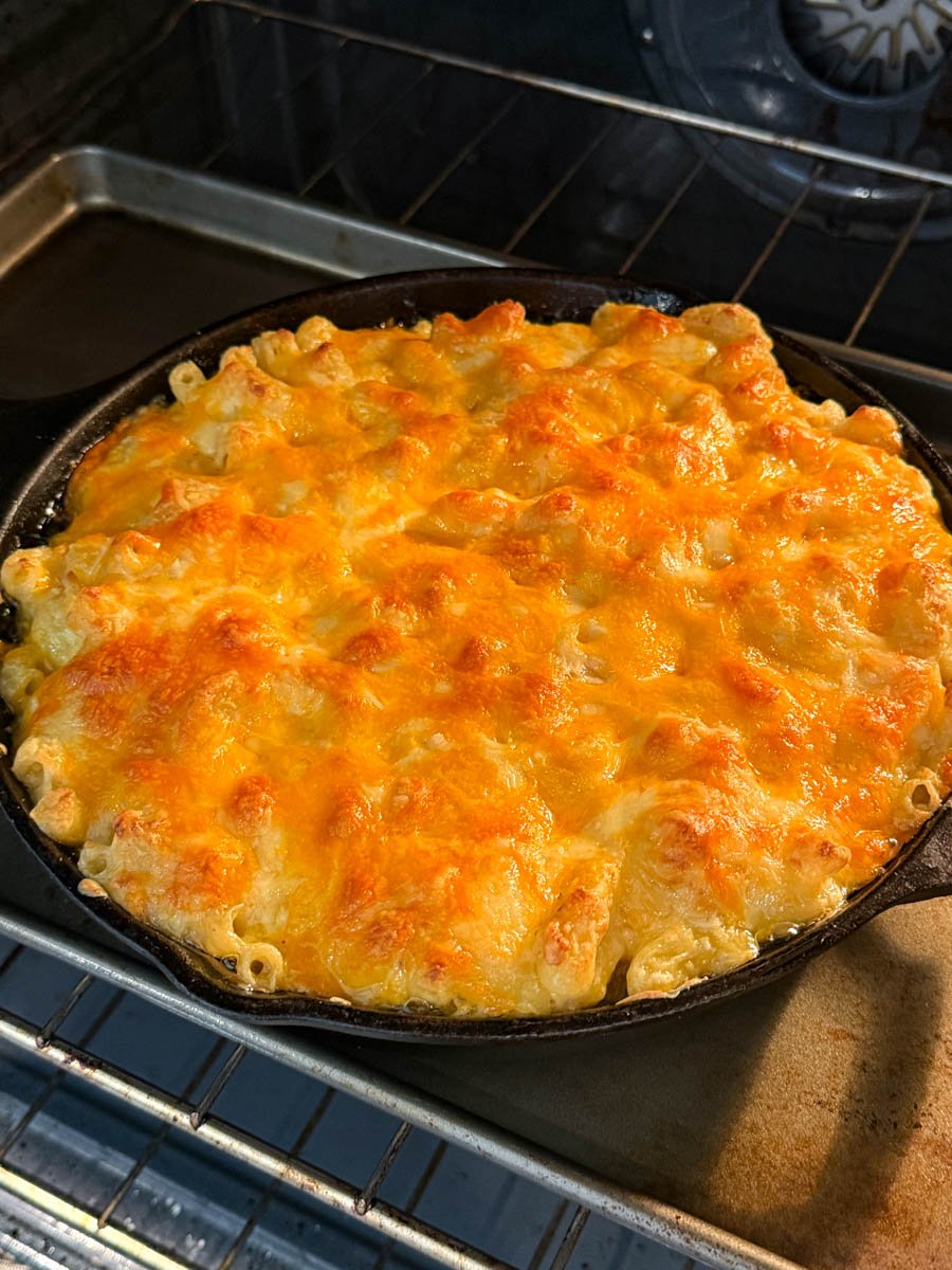 Southern soul food baked mac and cheese bubbling in the oven inside a cast iron skillet, with cheese browned and slightly crisp on top.