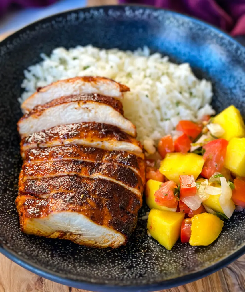 blackened chicken breasts with rice and mango salsa in a black bowl