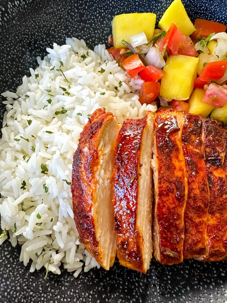 blackened chicken breasts with rice and mango salsa in a black bowl