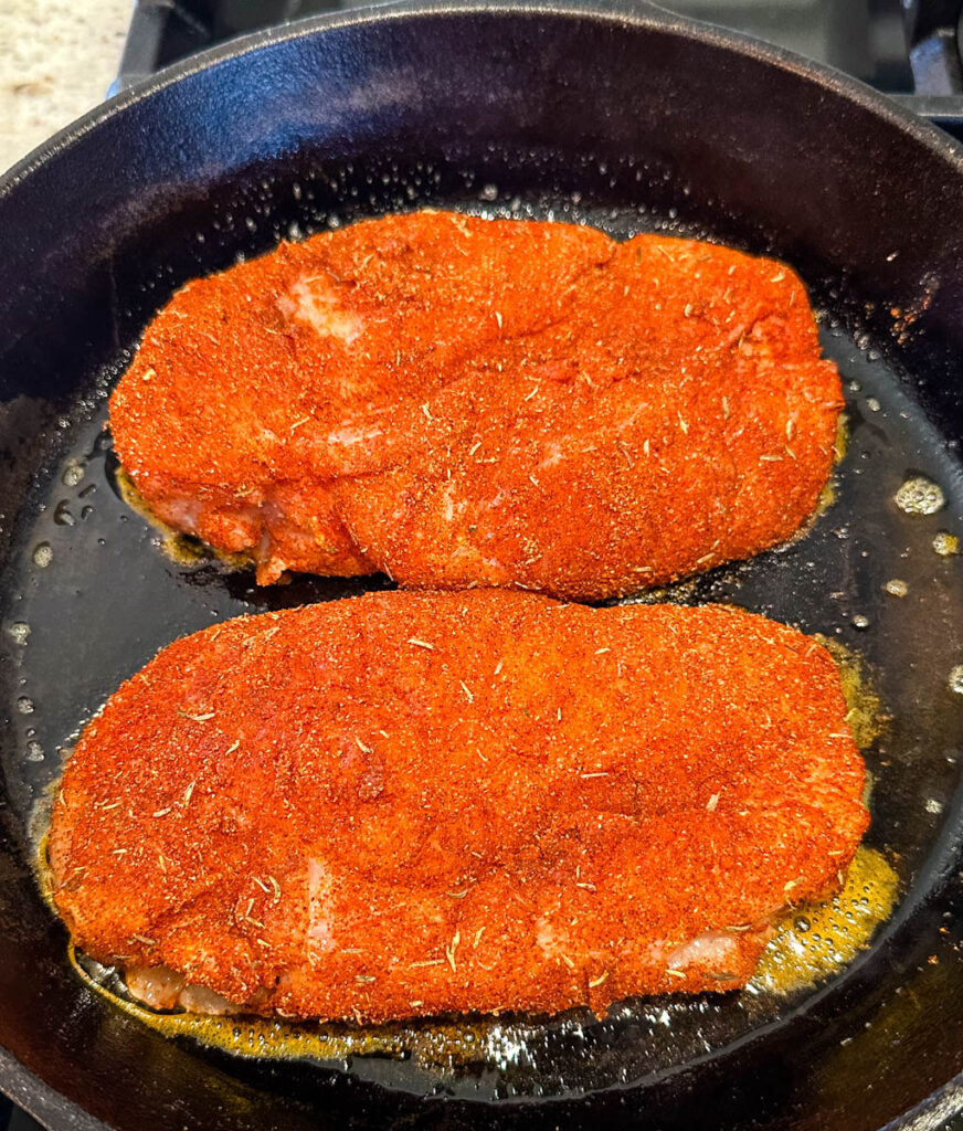 raw chicken breasts seasoned with blackening seasoning in a cast iron skillet