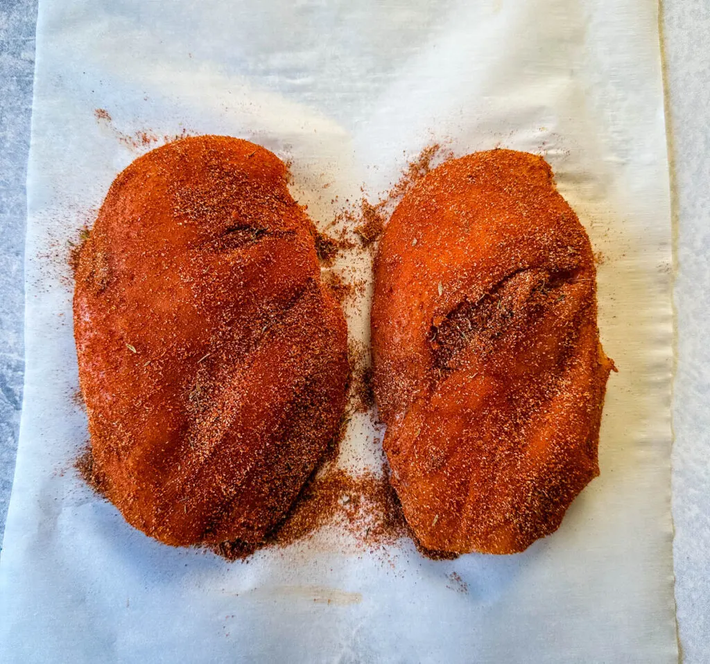 raw chicken breasts seasoned with blackening seasoning on parchment paper