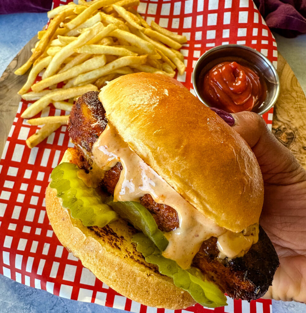 person holding blackened chicken sandwich on a bun with spicy mayo on a plate with fries