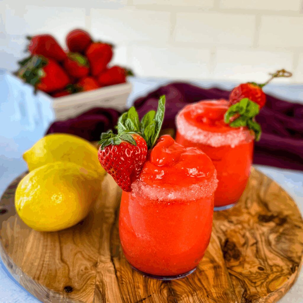 frozen strawberry lemonade in glasses garnished with fresh strawberries and fresh lemons