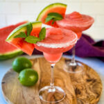 frozen margaritas in a sugar rimmed lined glass with fresh watermelon and limes