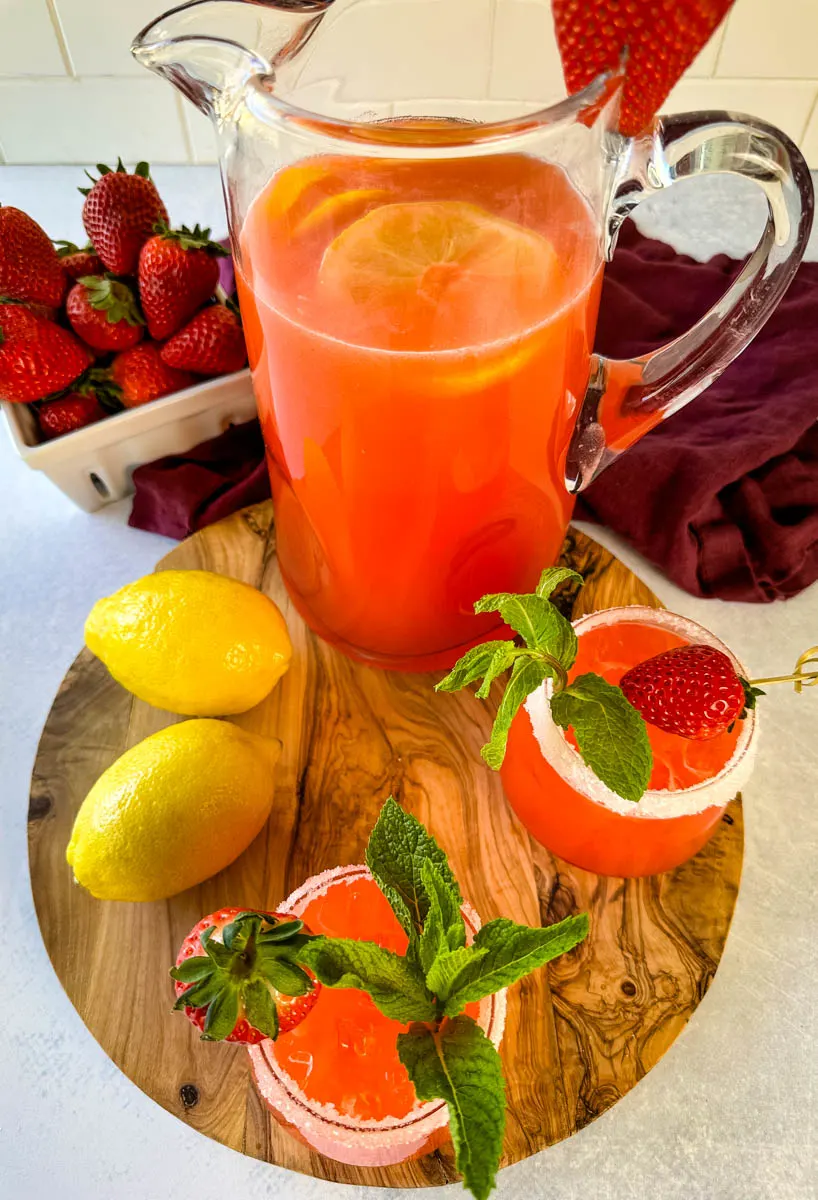 strawberry lemonade in a glass pitcher and glasses garnished with fresh strawberries and lemons