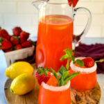 strawberry lemonade in a glass pitcher and glasses garnished with fresh strawberries and lemons