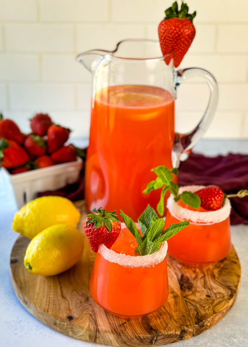 strawberry lemonade in a glass pitcher and glasses garnished with fresh strawberries and lemons