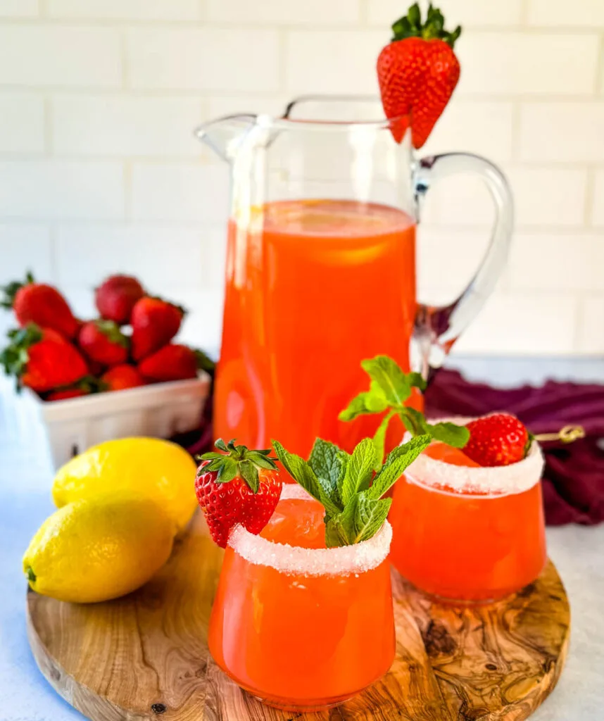 strawberry lemonade in a glass pitcher and glasses garnished with fresh strawberries and lemons