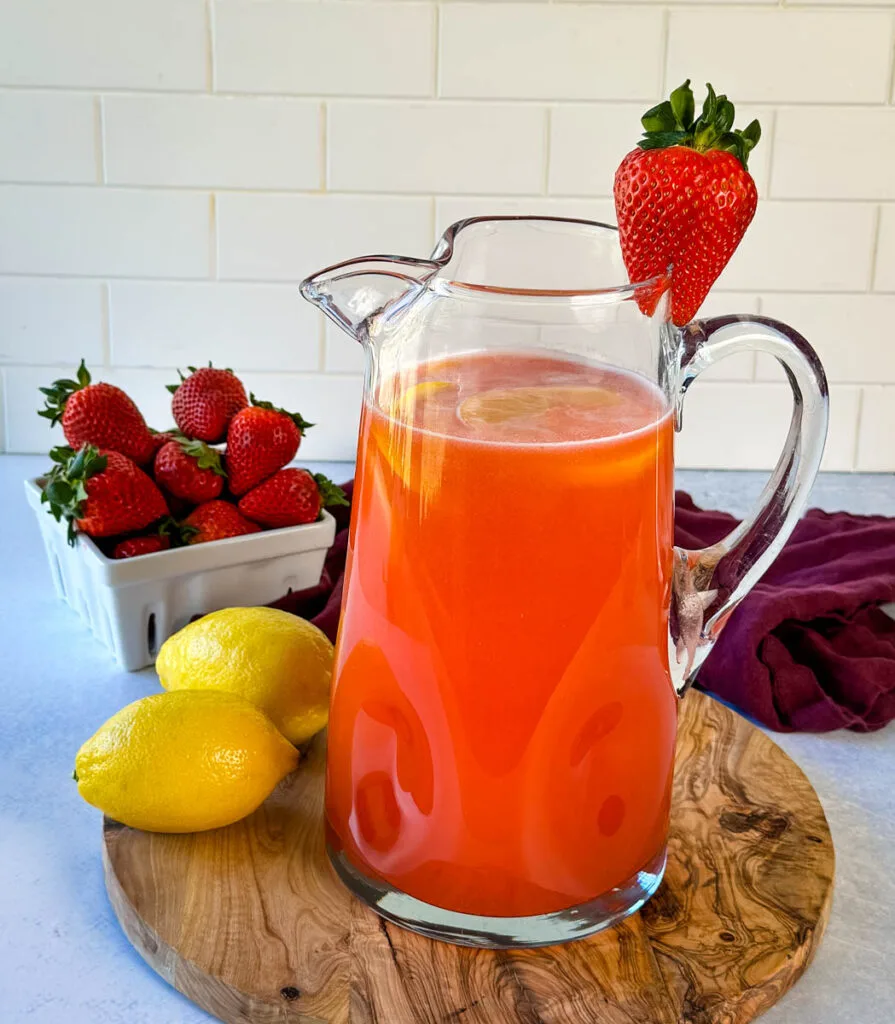 strawberry lemonade in a glass pitcher garnished with fresh strawberries and lemons
