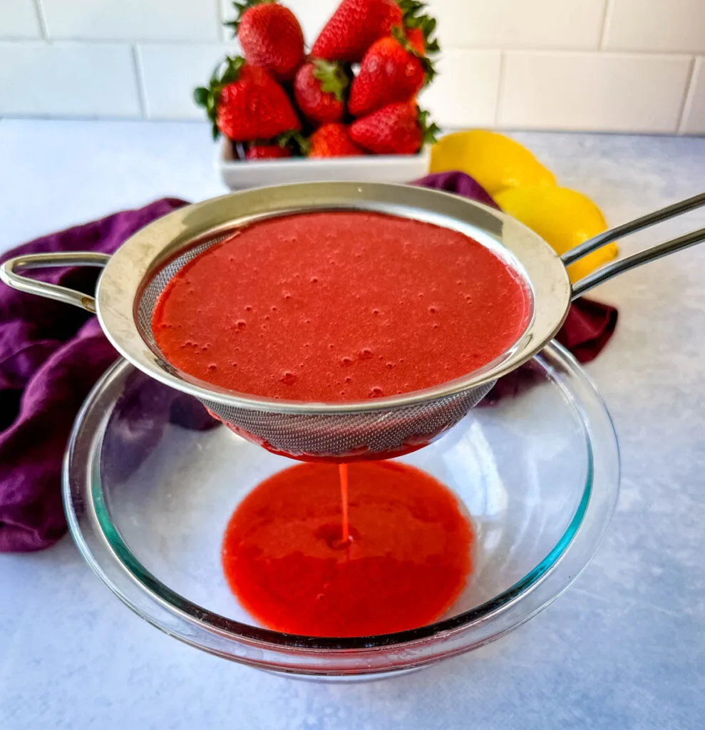 blended strawberries poured into a strainer and glass bowl