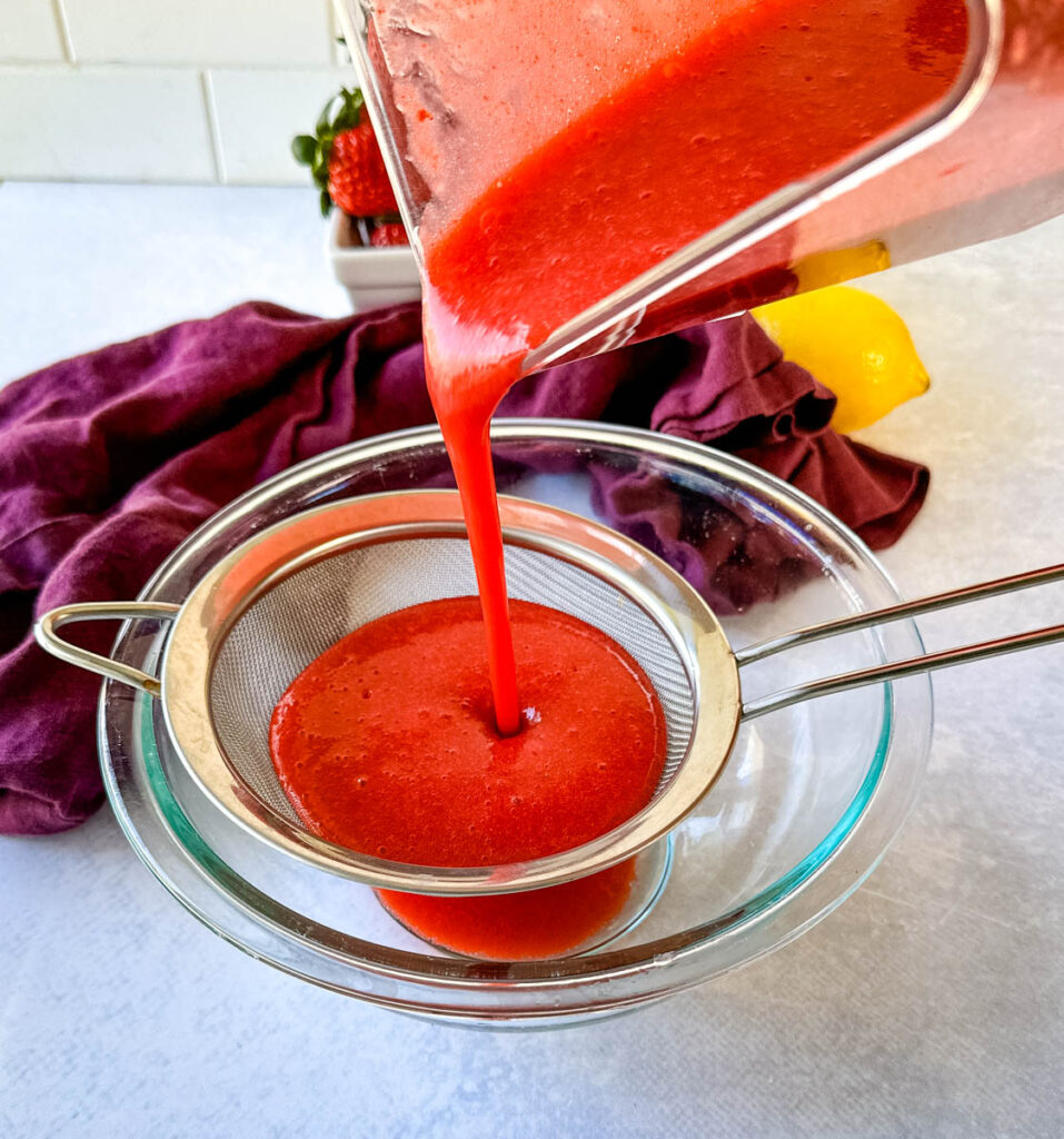 blended strawberries poured into a strainer and glass bowl