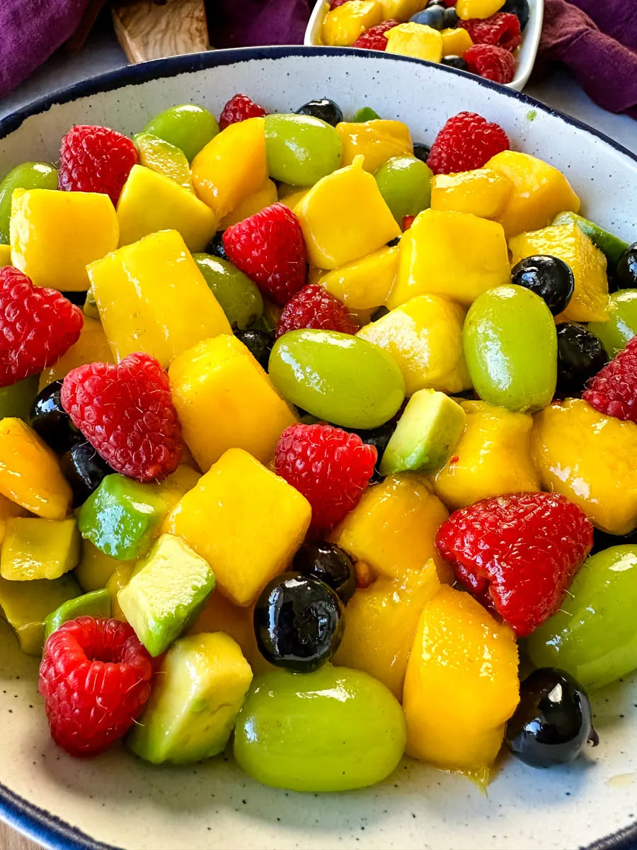 mango fruit salad with raspberries, blueberries, grapes, and avocado in a white bowl