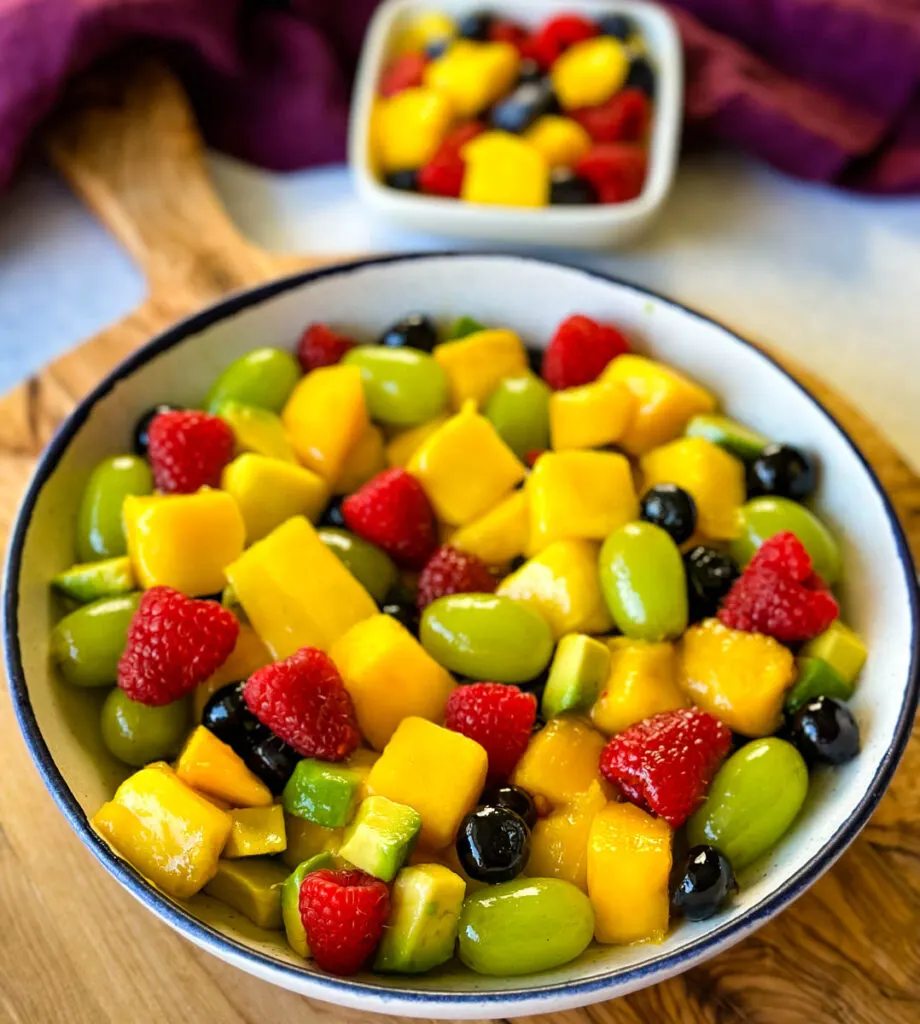 mango fruit salad with raspberries, blueberries, grapes, and avocado in a white bowl