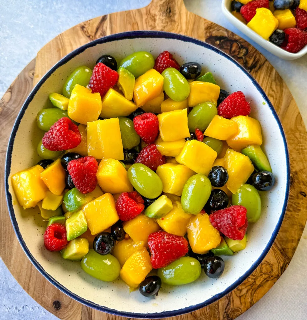 mango fruit salad with raspberries, blueberries, grapes, and avocado in a white bowl