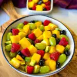 mango fruit salad with raspberries, blueberries, grapes, and avocado in a white bowl